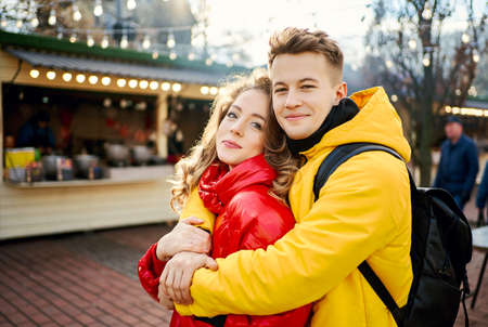 romantic couple looking in to the camera an smilling, young man in yellow down jacket embracing his girlfriend. spending time together in the city, having a date. urban romantic portrait. Romantic, love and Valentine's Day concept.の写真素材