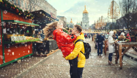 Young couple having fun together at snowy day and looking happy, handsome young man carrying his girlfriend while walking on the street. spending time together, having a date. urban background. Romantic, love and Valentine's Day concept.の写真素材