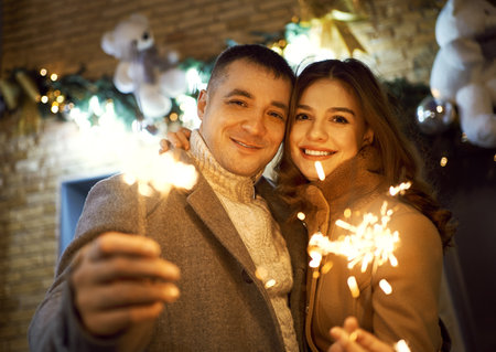 bright portrait of romantic couple smiling to the camera, with sparkle in hands, standing against bright holiday decorations. Spending time together at holidays, having a date. urban romantic portrait. Romantic, love and Valentines Day concept.の写真素材