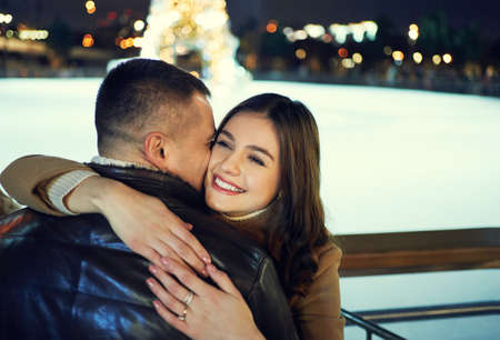 portrait of beautiful smiling woman embracing boyfriend and looking happy, standing against bright holiday decorations. happy moments together. Romantic, love and Valentines Day concept.の写真素材