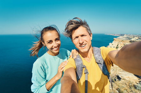 young man and woman tourist making selfie and smile to the camera on cliff edge with beautiful sea...