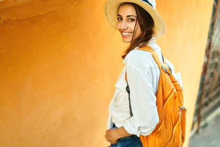 attractive tourist woman in straw hat, white shirt smiling to camera, standing against bright orange wall in tourists city. enjoying summer vacation in Europe, Mediterranean. Tourism and travelの写真素材