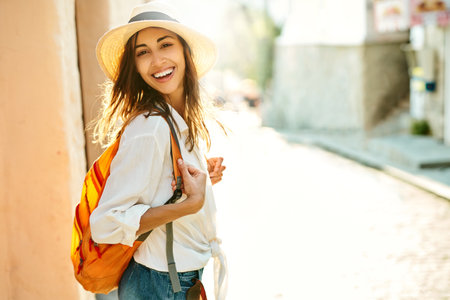 portrait joyful tourist woman walking ancient street, turning around to camera. Attractive girl in straw hat, white shirt enjoying vacation in Europe. Tourism and travel concept.の写真素材