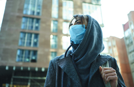 Woman in hood wearing protection face mask for prevention coronavirus, standing in city street with...