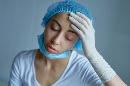 Tired nurse in uniform feeling sick, getting illness after receive patients in hospital. Concept pandemic outbreak, coronavirus disease, COVID 19の写真素材