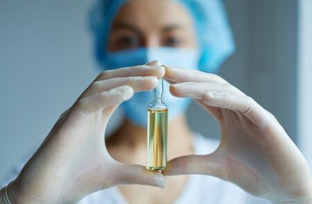 Close-up ampule with liquid drug in hands in gloves. doctor or scientist in laboratory blurred on background. Prevention, immunization and treatment from corona virus, flu, infection.の写真素材