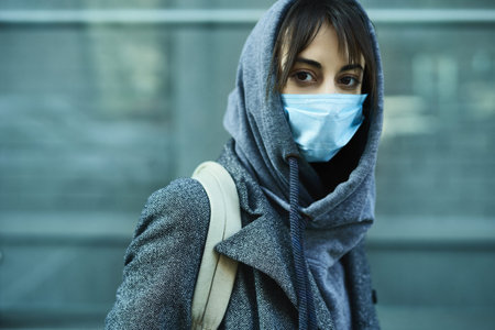 Coronavirus pandemic in city. Portrait woman in hood wearing face mask for protection of...