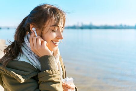 closeup portrait young pretty woman using Wireless Earphones outdoors. young beutiful woman walks on beach at sunny spring day and listening music by Wireless Tws Earphoneの写真素材