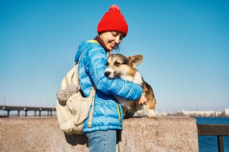 Smiling girl taking free time with her dog outdoors, dog walking. Loving young woman stroking and embracing cute Corgi dog at sunny spring dayの写真素材