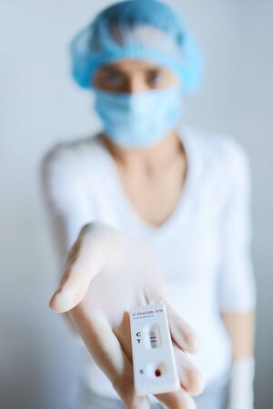 doctor or nurse in face mask reaching hand to camera with lab card rapid test for viral disease COVID-19. Test showing positive result. Diagnosis of coronavirusの写真素材
