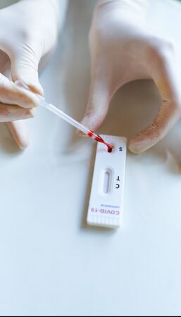 close-up doctor or nurse hands in gloves making rapid blood test for viral disease COVID-19, 2019-nCoV, dripping blood on lab card kit test. Testing for presence of coronavirus.の写真素材
