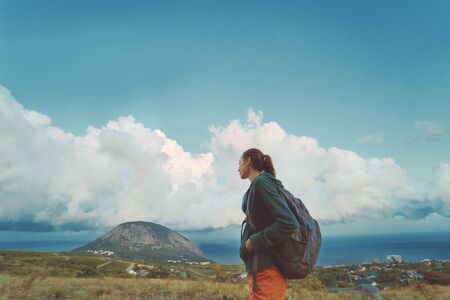 Traveler woman with backpack relaxing and enjoing serene view mountain, sky and seascape. Travel Lifestyle wanderlust adventure concept summer vacations outdoors alone, calm and freedomの写真素材