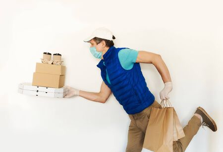 Delivery man in uniform face mask gloves carrying many cardboard boxes, running and hurrying to deliver takeout food. Food delivery service or shopping order online.の写真素材