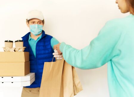 Delivery during quarantine. Courier in uniform face mask gloves giving food order to woman to home. Takeout food, online order, deivery to homeの写真素材