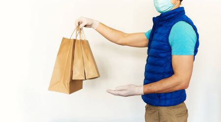 Courier in uniform face mask gloves reaching out hand with paper packages or bags n front of white background. takeout meal, deivery to home, food delivery, shopping order online.の写真素材