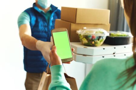 first-person view of woman using smarthone for ordering online, receiving takeout food from delivery man. Courier holding paper boxes and containers. Delivery food service during quarantineの写真素材