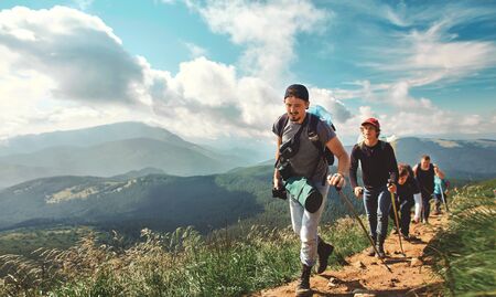 Company of friends travelers walking on the mountain hill with grass field, hiking in mountains, enjoying beautiful scenery. traveling lifestyle, people in nature, wild natureの写真素材