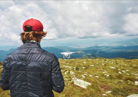Rear view man controling quadcopter drone with digital camera outdoors. Drone flying over moutains landscape, takes pictures of beautiful scenery of wild natureの写真素材