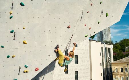 Sports girl climber climbing on artificial rock wall in outside climbing gym. Strong woman making hard move on tough sport route. extreme sports, strength, conquering and active lifestyle concept.の写真素材