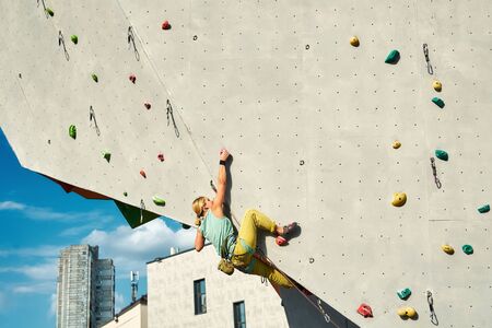 Young woman rock climber climbing on artificial rock wall in outside climbing gym. sports woman working out on extrime sport route. strength, conquering and training conceptの写真素材