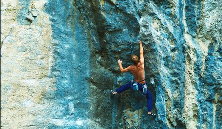 Rear view of strong man rock climber climbing the challenging route on the bright colorful rock cliff, making hard move. Power, strong, concentrated, strength conceptの写真素材