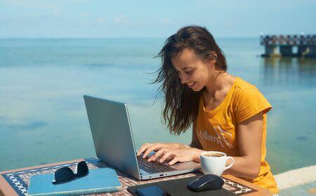 female freelancer working by the sea, using laptop computer. Freelance work concept, technology, travel and vacationの写真素材