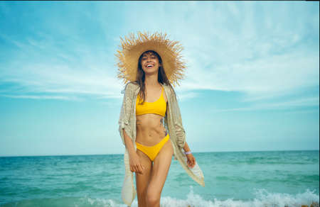 Joyful happy travelr woman in fashionable swimwear and straw hat goes on camera wiht sea view on background. tourism and sea resort, latin woman on vacationの写真素材