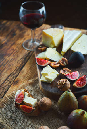 Delicious cheese mix with figs and walnuts. Tasting dish on a wooden cutting board. Food for red wine. Autumn food and snacks conceptの写真素材