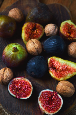 fresh sweet figs whole and sliced with walnuts on craft wooden cutting board. Autumn seasonal...