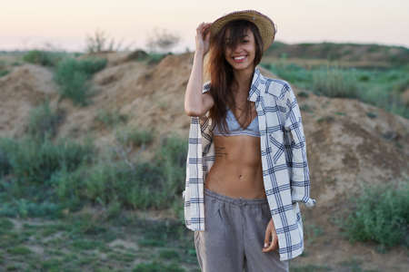Beautiful stylish woman in hat with perfect slim body and naked belly posing in desert, smiling to camera, natural beauty, woman and natureの写真素材