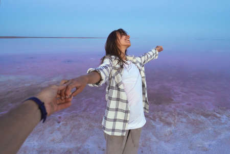 first person view, POV delighted woman on colorful dreamy lake, girl holding mans hand while walking on salt beach. Domestic traveling, beautiful nature landscape. Unfocused image.の写真素材
