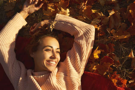 carefree woman lying on fallen leaves and enjoying warm sunny weather at autumn park.の写真素材
