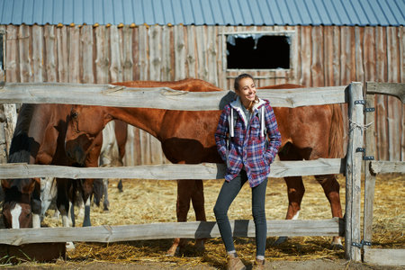 American female breeder standing by stable with horses on countryside farm or ranch. Animals, friendship and hobby concept.の写真素材