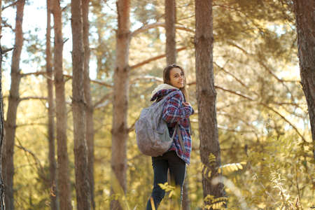 tourist woman with backpack in forest, smiling and turning around to camera. Travel lifestyle and hiking conceptの写真素材