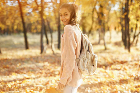 Pretty girl walking at autumn park with fallen leaves in hands, colorful foliage and sunlights on background. Autumn walk conceptの写真素材