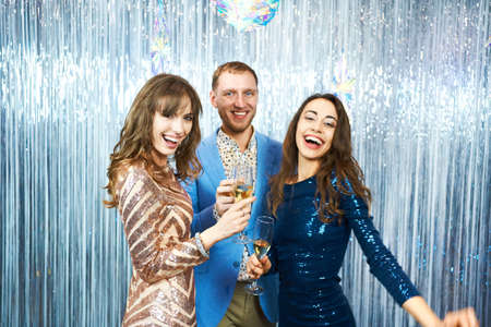 group of happy celebration people on silver shiny background, holds glasses of champagne. focus on blonde girlの写真素材