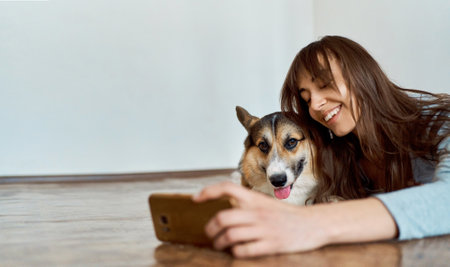 Woman with charming smile lying on floor in living room with pet and making selfie photo. Spend time together at home. Focus on dogの写真素材