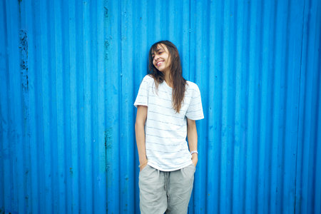 Young latin woman standing by bright blue wall, looking to side with smile to copy spaceの写真素材