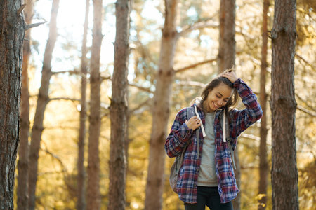 cheerfulness casual woman at fall forest with sun rays on background, feeling good hiking in woods. concept activity and adventure outdoorsの写真素材
