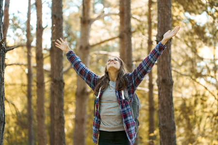 Delighted positive woman with raised hands enjoying beautiful nature in forest. Concept vacations outdoor harmony with natureの写真素材