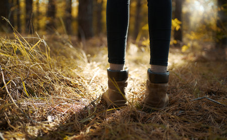 Wanderlust photo woman legs in hiking leather boots forest glade, sun rays highlighting way forwardの写真素材