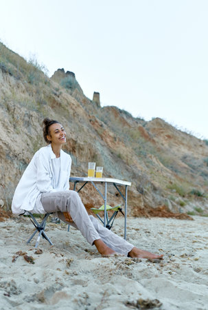 Summer beach camping. Carefree woman sitting on camping chair and looking away. Concept authentic people, candid portraitsの写真素材