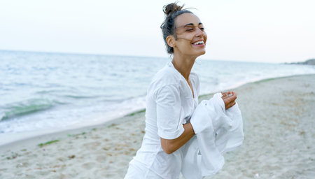 Candid emosional portrait laughing young woman at beach. Latin tanned girl taking off white shirt.