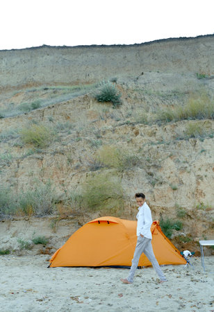 Full length shoot summer girl walking on sandy beach near orange tent, enjoying camping life during vacationの写真素材