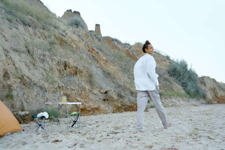 Rear view joyful woman walking on summer beach along cliff, enjoying camping life and wild natureの写真素材