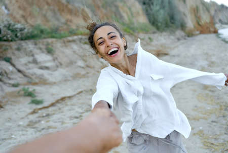 Motion portrait laughing woman holding hand boyfriend and whirling by wild beach, expressive emotions. Real life authentic peopleの写真素材