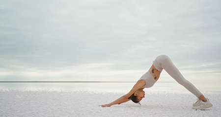 Active fit woman practicing yoga outdoors, doing downward facing dog pose on salt lake coast beautiful sceneryの写真素材