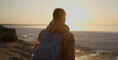 Back view man traveler with backpack walking along salt lake coast and meeting sunrise at deserted...