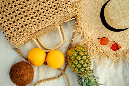 Beach summer female fashion outfit and tropical fruit flat lay. Close-up straw hat, straw bag, sunglasses, pineapple, coconut, grapefruit on blanket.の写真素材