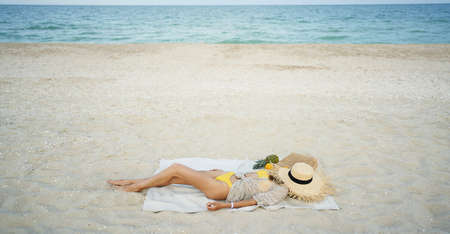 relaxing woman lying and sunbathing at beach, beach accessories and fresh fruit on blanketの写真素材